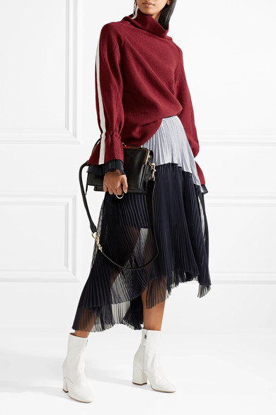 Sacai 对混搭面料和精美设计的热爱继续主宰 2017 秋冬系列。秀场中的这款羊毛混纺毛衣双袖带有运动风罗缎条纹，袖口点缀着褶裥欧亘纱边饰，调整抽绳还可展示更为夸张的喇叭袖造型。不妨借鉴秀场装扮，将半边衣摆束入…