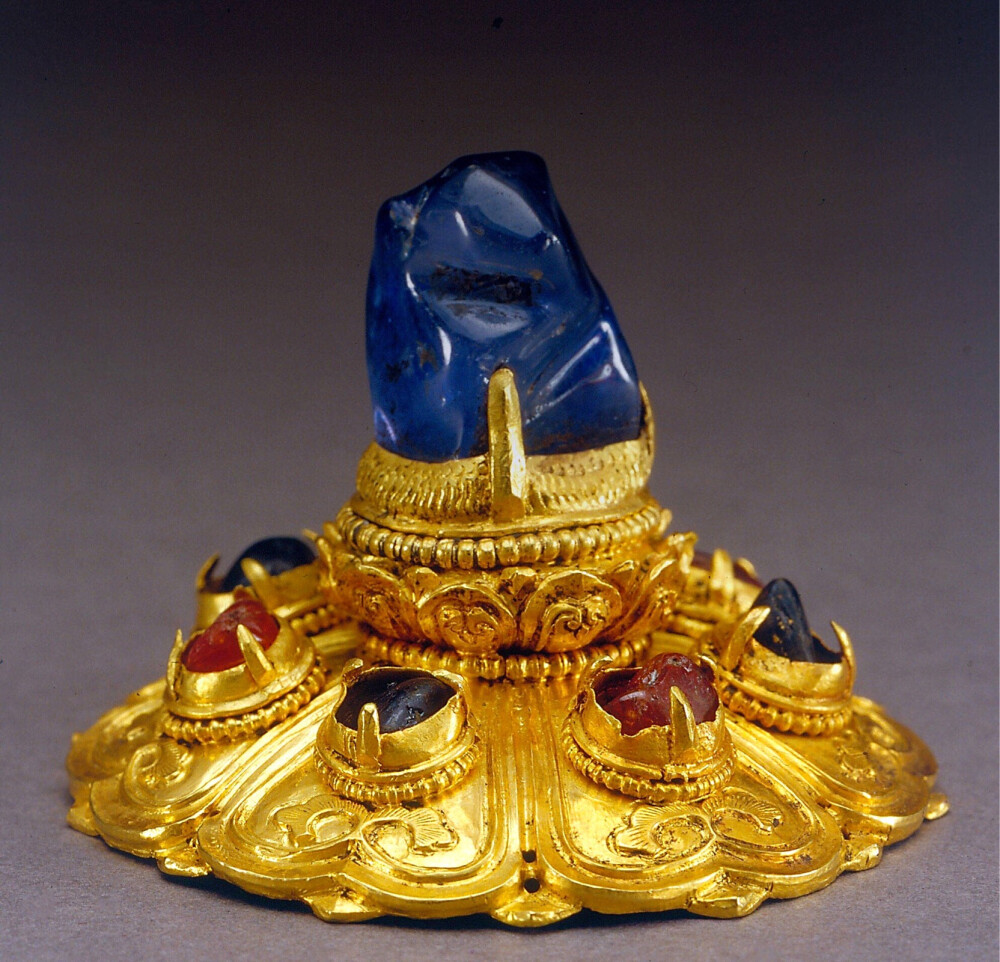 金镶蓝宝石帽顶,现存宝石7颗,金质底座分为三层:下层为1朵绽开的七
