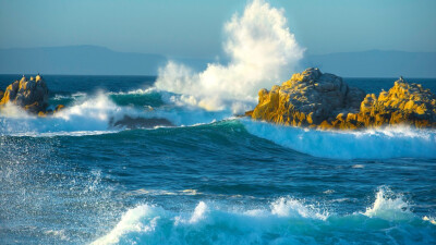 汹涌的海浪风景图片高清宽屏壁纸。浩瀚无边的湛蓝的海洋，一道道波浪不断涌来，撞击在岩石上，发出了天崩地裂的吼声，喷溅着雪白的泡沫。 