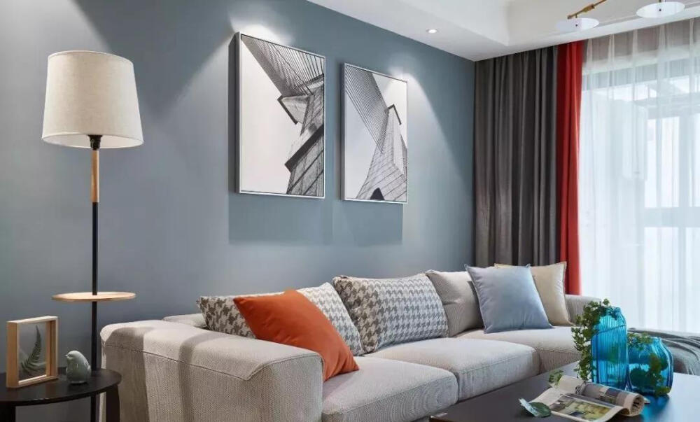 客厅整体以冷色为基调，舒适的布艺沙发搭配蓝灰色背景墙，一抹橘色的点缀，造成视觉上的跳跃