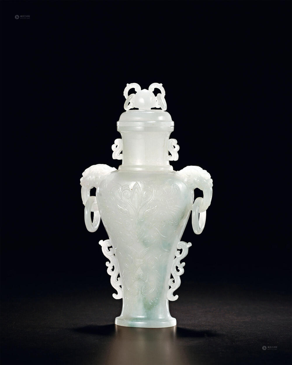 清 翡翠雕兽面纹双耳衔环盖瓶，高22cm。盖瓶翡翠质地，造型古拙。子母口相合紧密；盖顶置圆钮抓手，双活环。瓶颈部微向内收。对称的两侧透雕灵芝衔环，腹部主题纹饰为兽面纹。瓶腹部内收，两侧雕蟠螭，并置二层台式底足。此瓶体形纤细隽秀，所选翡翠料晶莹通透，翡翠高冰种，无疑是一件宫廷陈设精品之作