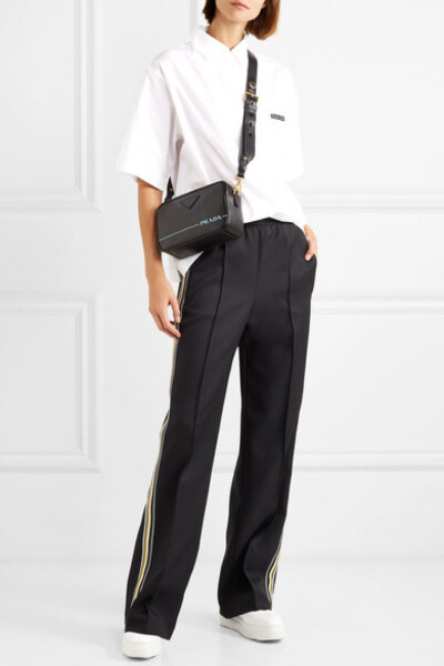 Prada 这款休闲裤侧面配有黄色和白色的条纹，其上印有 “Prada Milano” 的蓝色字样，品牌出身一目了然。单品背面配有拉链口袋，松紧腰身则保证灵活舒适。裤腿饰有平整的缝线压痕——“借用”精裁裤经典的裤线元素，…