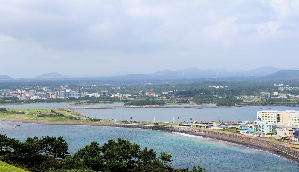  远处的蓝海泛着粼粼微光，那股海腥味似乎还若有若无地停驻在鼻尖。洁白柔软的云层像是从岛上青翠的群山生长出来，温柔地投下一片阴影。是济州啊