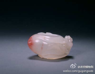 【玛瑙桃形小水丞】清，高3.5cm，口径2.4－3.2cm。清宫旧藏。水丞白玛瑙质，半透明，局部有红色，作桃形，器内空，器外装饰镂雕的桃枝、桃叶，以巧做技法使料中的红色恰好置于桃尖上，生动逼真。