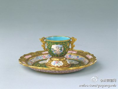 【金胎画珐琅杯盘】清乾隆，通高15.8cm，杯口径4.5cm，盘口径14cm。此套杯盘的制作，同时应用了画珐琅和錾胎珐琅两种珐琅器制造工艺，錾刻的花纹金光闪烁，图案用色丰富。其图案主题为西洋风景和人物画……