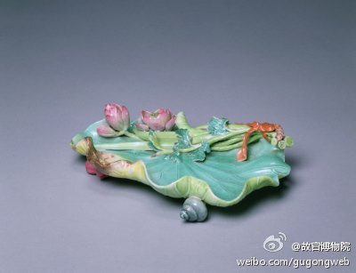 粉彩雕镶荷叶香橼盘，清乾隆，高3.8cm，长15.7cm，宽10.5cm。清宫旧藏。盘呈荷叶形，叶面翻卷起伏，叶梗从叶后过枝而上，叶面边缘处贴塑含苞待放的花苞与莲实，莲蓬中有可活动的莲籽，器底粘有田螺和菱角形足。底书…