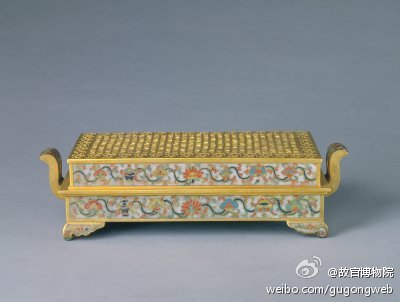 掐丝珐琅八宝纹长方熏炉，明万历，御用监制造，通耳高9.1cm，盖面26.8×14.4cm，底面25.5×13.2cm。熏炉呈长方形，朝冠式双耳，垂云式四足。四壁以灰白色珐琅釉为地，饰掐丝彩釉八宝勾莲纹，盖面无釉，作铜鎏金镂空纹饰，边框为一周“卐”字纹，边框内饰绣球纹。