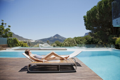 Woman sunbathing on lounge chair next to luxury swimming pool with mountain view by Caia Images on 500px