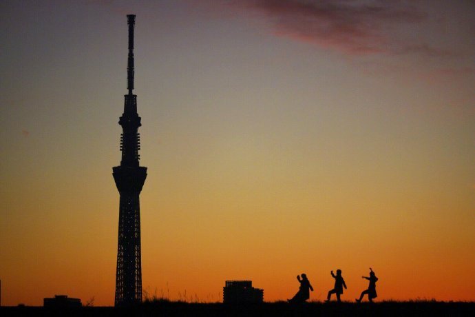 一位推主拍夕阳下的东京天空树，刚好遇到几个女学生从河堤上走过，还注意到了他的镜头，即兴摆起pose来...突然觉得青春真美好，生活真美好