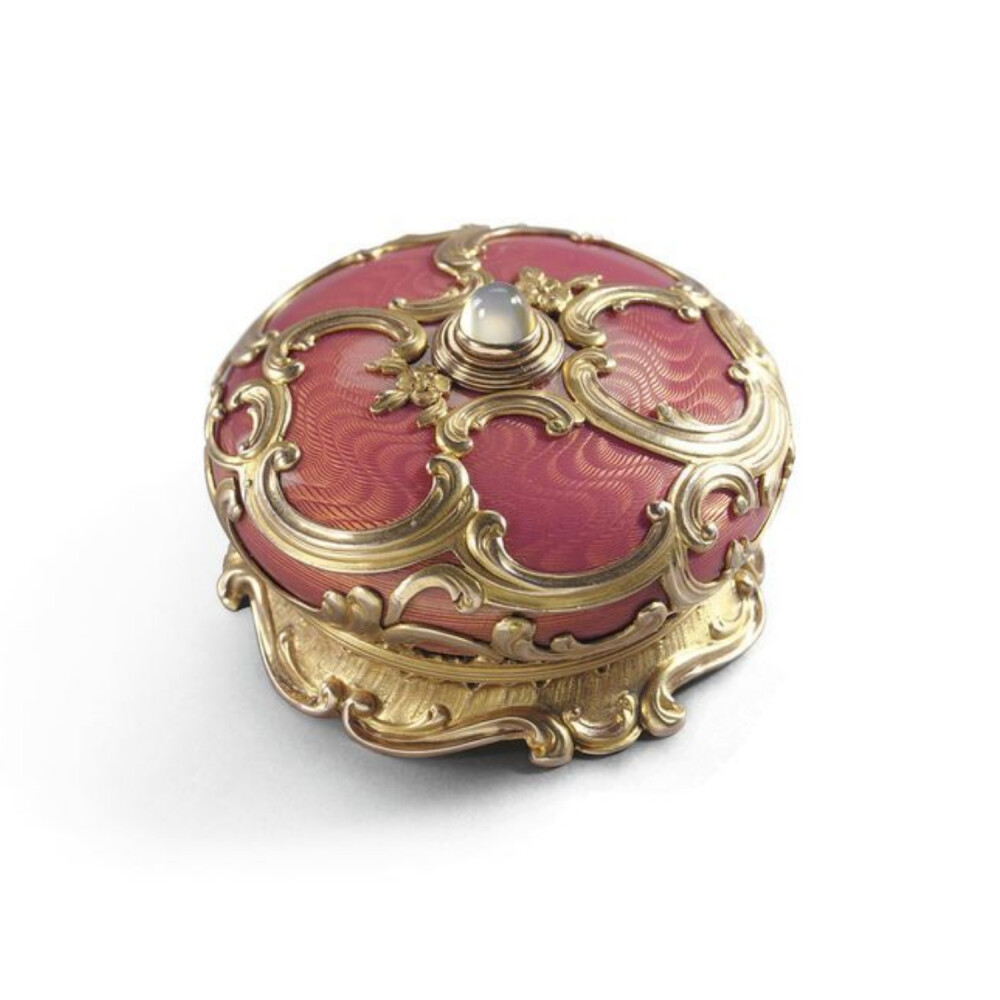 A Fabergé gold and enamel bell push, Workmaster Henrik Wigström, St Petersburg, 1908-1917. In Rococo taste, of circular cushion form, the surface enamelled in translucent rose Pompadour over moiré engine-turning, overlaid with gold scroll and floral cagew