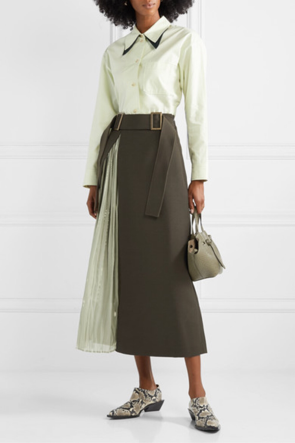 REJINA PYO 擅长为日常服饰融入新意。这次，她将羊毛混纺斜纹布与亮泽的灰绿色褶裥缎布巧妙拼接，再添上可调式搭扣腰带，打造出这款别致而又实穿的 “Evie” 半身裙。在个人品牌的 2019 秋冬时装秀上，设计师便是身穿一款类似单品为大秀闭幕，你不妨从当日造型中借鉴一二，将女衫束入裙腰并搭配踝靴。