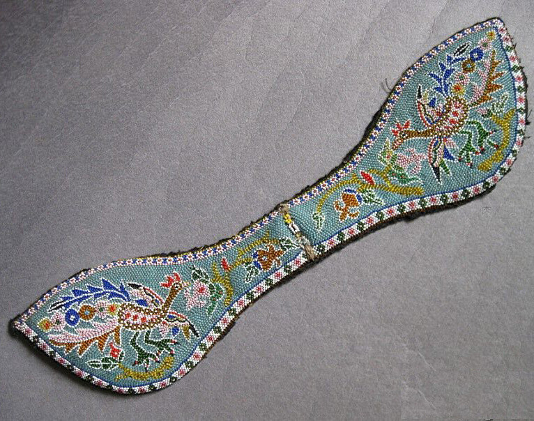 上缘边框线分别以金黄色和粉红色米珠界出，边框内等距间隔绣出六瓣红心白色梅花，花与花之间用蓝色“工”字形作为间隔，花和间隔纹饰计有116个。下缘边框线则分别以蓝色和褐色米珠界出，边框内则等距间隔绣出菱形红心粉色花朵和粉心绿色花朵，花与花之间用白色古币文“五”字形作为间隔，花和间隔纹饰计有136个。一周边框内花和间隔纹饰共计252个。自上至下最宽处的米珠排列线条达70多道。中部以蓝色米珠打底，以白色米珠勾出图案轮廓，用五光十色的米珠绣出主题图案——双凤衔石榴纹，寓意富贵多子。整个双凤衔石榴主题纹饰共由约180个大小不同、形状各异的色块有机组合而成，所用各色米珠（不含底色米珠）约有5000颗。