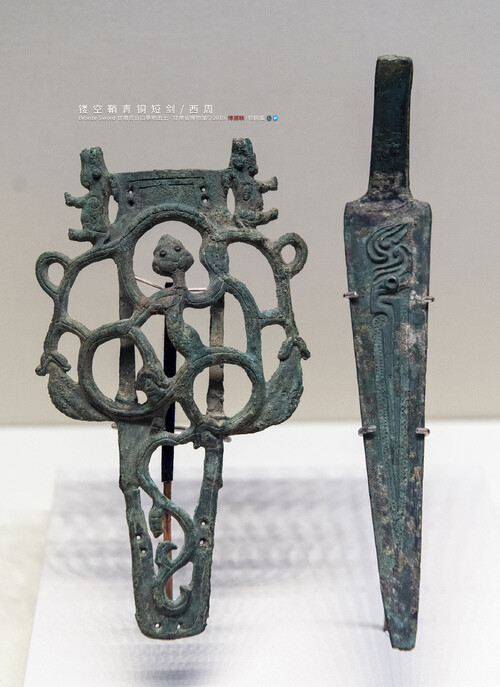 镂空鞘青铜短剑 西周 甘肃灵台白草坡出土 甘肃省博物馆藏
Bronze Sword/The Western Zhou Dynasty(1046-771B.C.)/Unearthed at Lingtai Baicaopo,Gansu China/Gansu Provincial Museum
剑身三角形 扁茎五格 两面饰斜角雷纹 镂空鞘饰蟠虺纹 鞘口饰一对犀牛 应为悬腰佩带