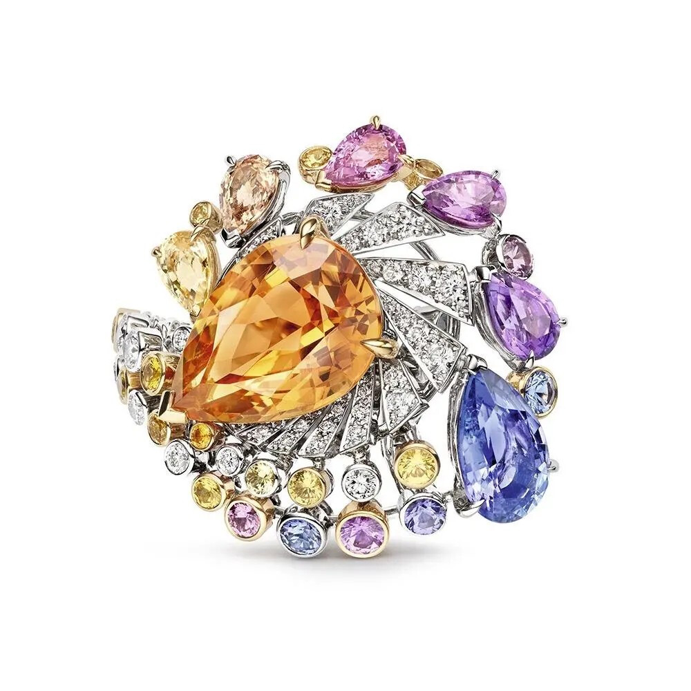 （Chaumet）尚美「Lueurs d&apos; Orage」戒指
主石为一颗8.72ct的水滴形切割帝王托帕石，点缀坦桑石、紫水晶、黄色蓝宝石、粉色蓝宝石、紫色蓝宝石和钻石。
戒指的灵感汲取自暴风雨下变幻莫测的天色，展现人类对天空的诗意想象，戒指名称在法语中正是意为「暴风雨」。缤纷的色彩亦对应着缤纷的天色，各色宝石的搭配展现了美好的自然。
戒面中央的帝王托帕石，拥有明快的橘黄色调。下方衬以漩涡状的辐射图案，模仿被风吹散的云层。外圈可以看到大小渐次的坦桑石、紫水晶、彩色蓝宝石，营造出雨滴从高空坠落的动态。