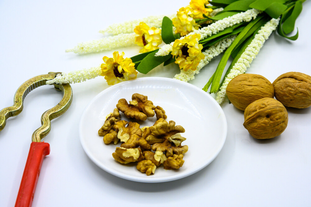 食品 食物 植物 果实 成熟的 特写 绿色食品 美味 零食 坚果 干果 核桃 核桃仁 膳食纤维 小吃 益智 亚洲 健康食物 有机食品 膳食 养生 滋补 营养 食材 生活方式 健康的 白色背景 白瓷盘 干果钳 简单背景
